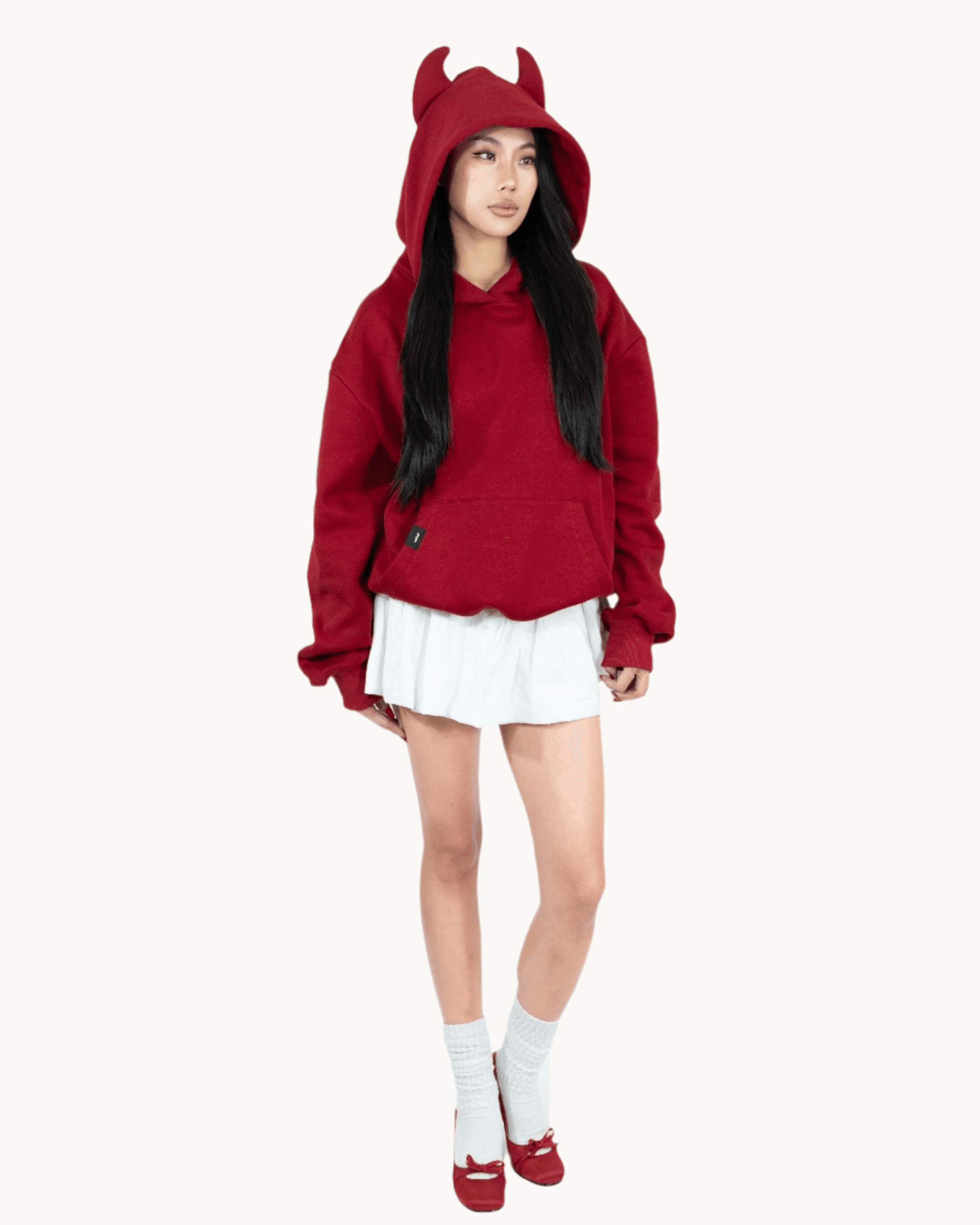 Woman in red devil horn hoodie, white pleated skirt, red shoes, and white socks