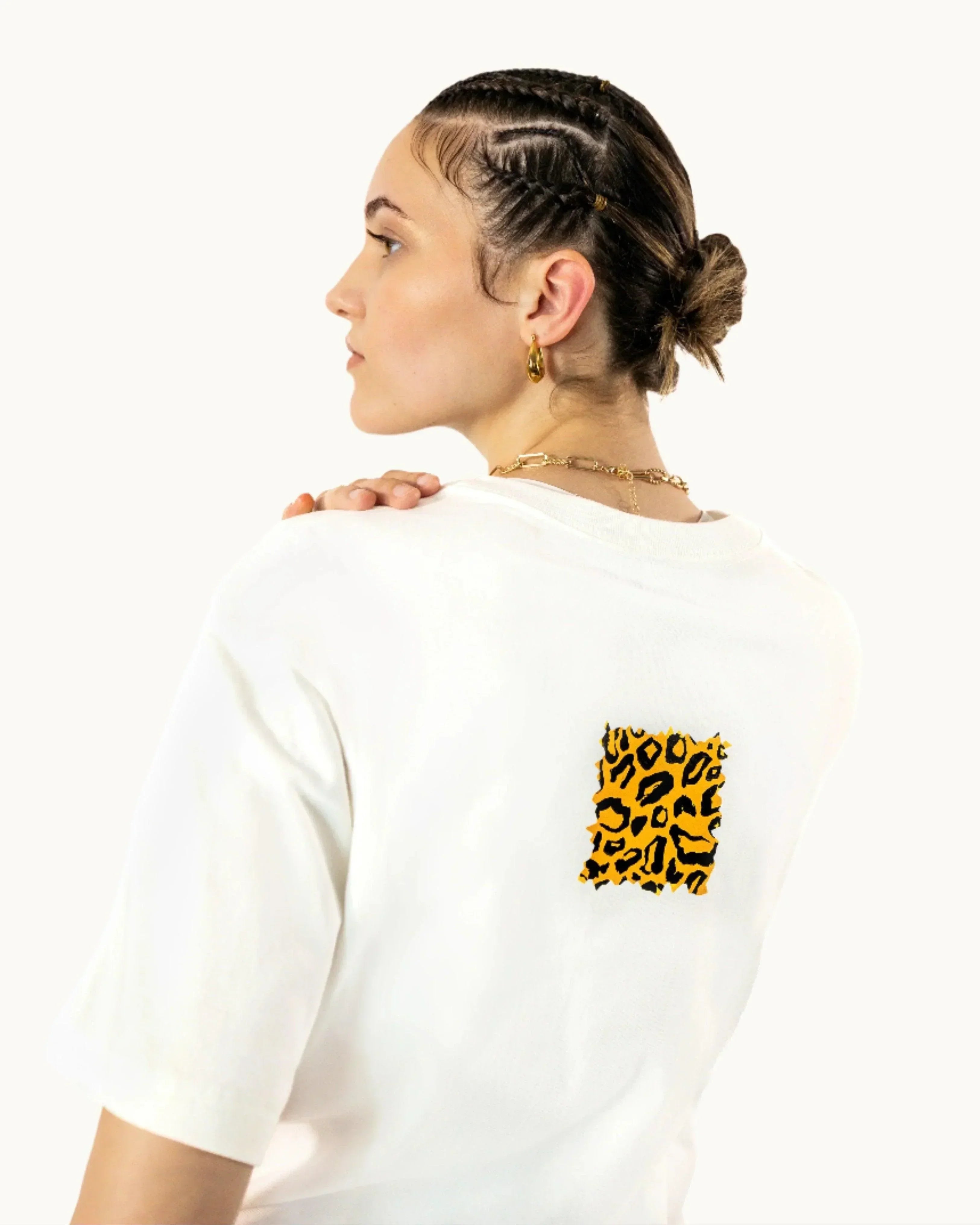 Woman in white t-shirt with yellow leopard print patch, gold jewelry, braided hair