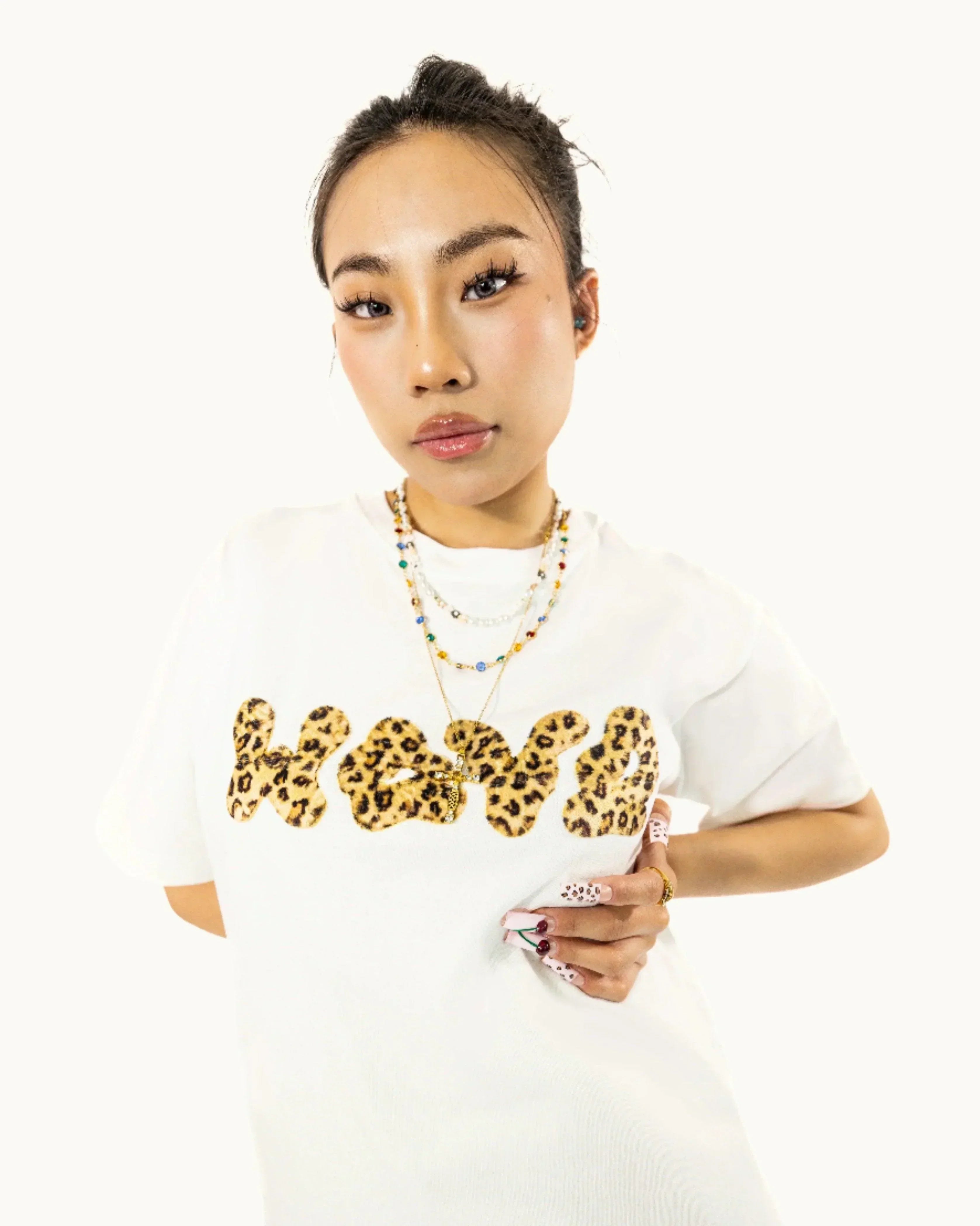 Woman in white t-shirt with leopard print 'love' text, layered necklaces, and patterned nails