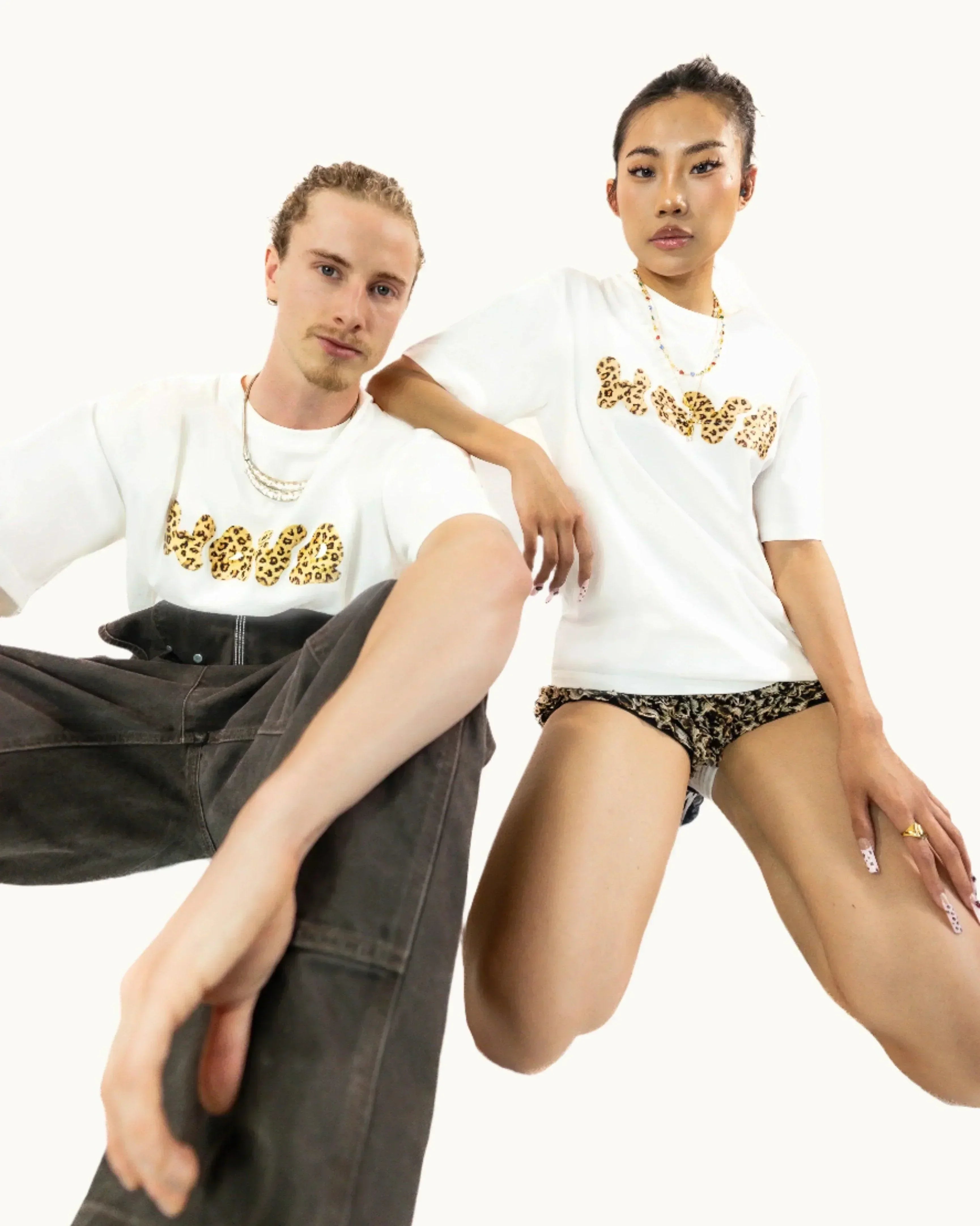 Two models wearing white t-shirts with leopard print text and animal print shorts against white background